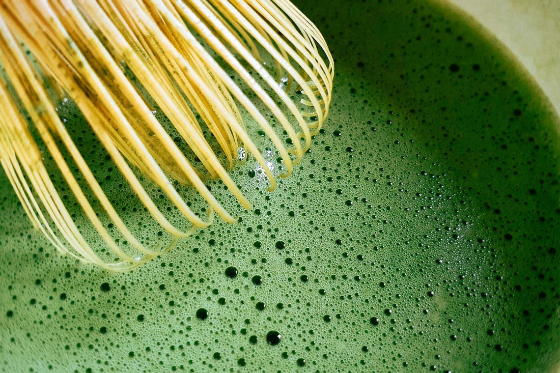 Bamboo whisk preparing ceremonial matcha green tea with fine foam during traditional matcha preparation