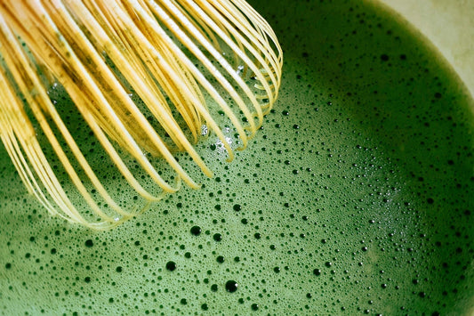 Bamboo whisk preparing ceremonial matcha green tea with fine foam during traditional matcha preparation
